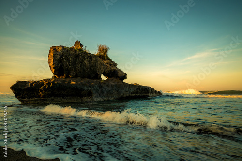 Amazing seascape. Sunrise at Yeh Gangga beach. Rock in the ocean. Natural hole in rock formation. Slow shutter speed. Long exposure with soft focus. Tabanan  Bali.