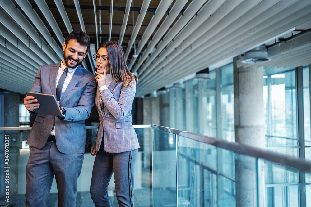 Smiling handsome caucasian businessman in suit showing to his female colleague results online auction for building they standing in. Smiling handsome caucasian businessman in suit showing to his female colleague results online auction for building they standing in.