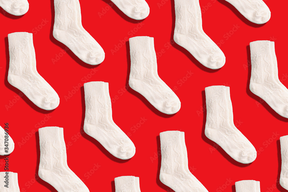 Pair of white woolen knitted socks pattern on red background. Top view. Copy space. Creative design for packaging. Christmas and New Year cozy holiday composition. Winter weather Pair of white woolen knitted socks pattern on red background. Top view. Copy space. Creative design for packaging. Christmas and New Year cozy holiday composition. Winter weather