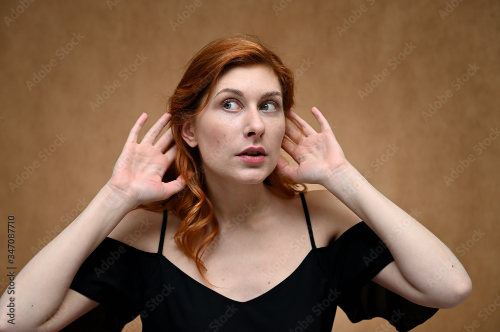 Close-up portrait of a young pretty woman with long red hair on a beige background. Model posing without makeup.