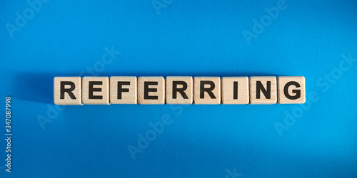 Referring - text concept on wooden cubes with blue background