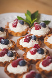 Homemade tartlets with vanilla cream and organic blueberries and raspberries, decorated with mint on a white plate. Delicious sweet dessert for a party or celebration.