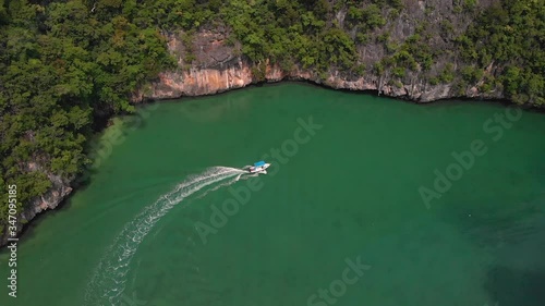 High drone view of a speed boat cruising into Pang Na Bay on Koh Yao Noi Island in Thailand; following, tilt-up and panning right. photo
