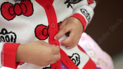 Closeup of little baby girl trying to button a sweater by herself - child development by learning to do things by themselves