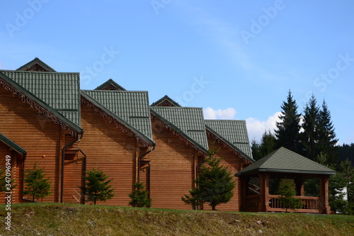 closeup of modern wooden houses with green metal tiles and a gazebo in a hotel on the background of fir trees and blue sky