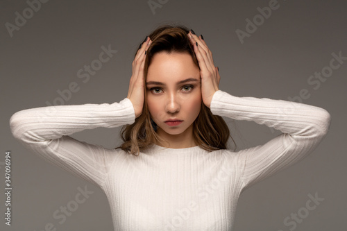 Portrait of beautiful young brunette girl touching her head feeling stress, on grey background