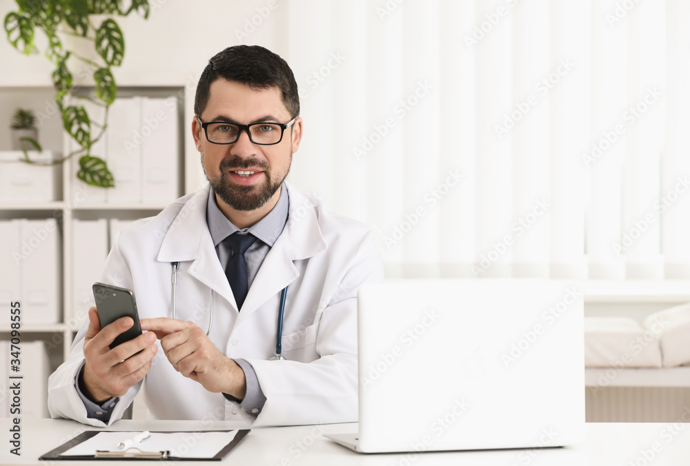 Male doctor with smartphone at table in office