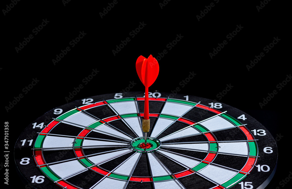 Red dart arrow hitting in the target center is Dart board on Black background Red dart arrow hitting in the target center is Dart board on Black background