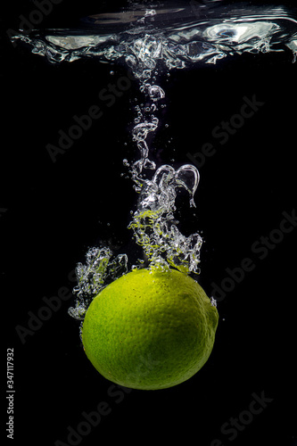 whole and sliced green lime falling under water with a splash and bubbles on a white or black background
