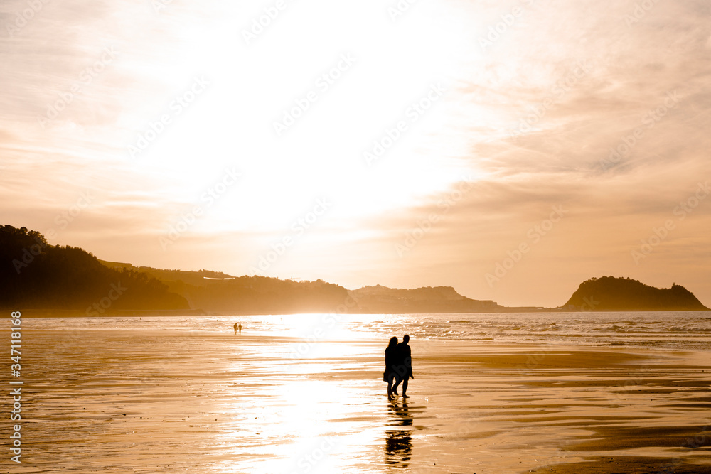 two people walking along the seashore in a beautiful orange sunrise