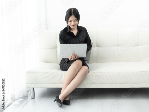 Asian woman in blank using laptop sitting on sofa at home, quarantine concept.