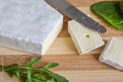 slices of brie cheese on wood cutting board with green salad leaves close up