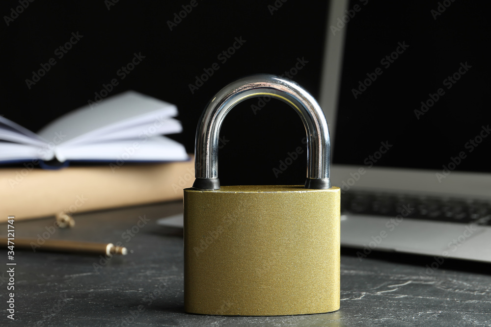 Naklejka premium Metal lock and laptop on grey table, closeup. Protection from cyber attack