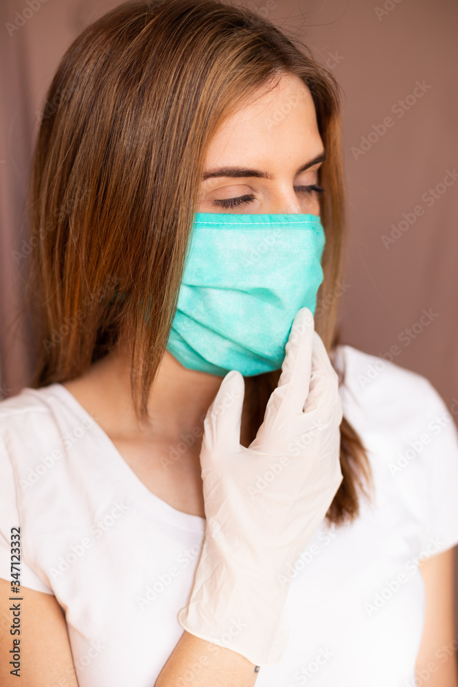 portrait of beautiful young woman wearing cotton green mask and white medical/surgical gloves on pastel background. She is adjusting mask. portrait of beautiful young woman wearing cotton green mask and white medical/surgical gloves on pastel background. She is adjusting mask.