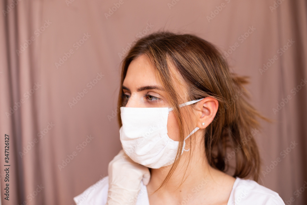 portrait of beautiful young woman wearing cotton white mask and medical/surgical gloves on pastel background. 