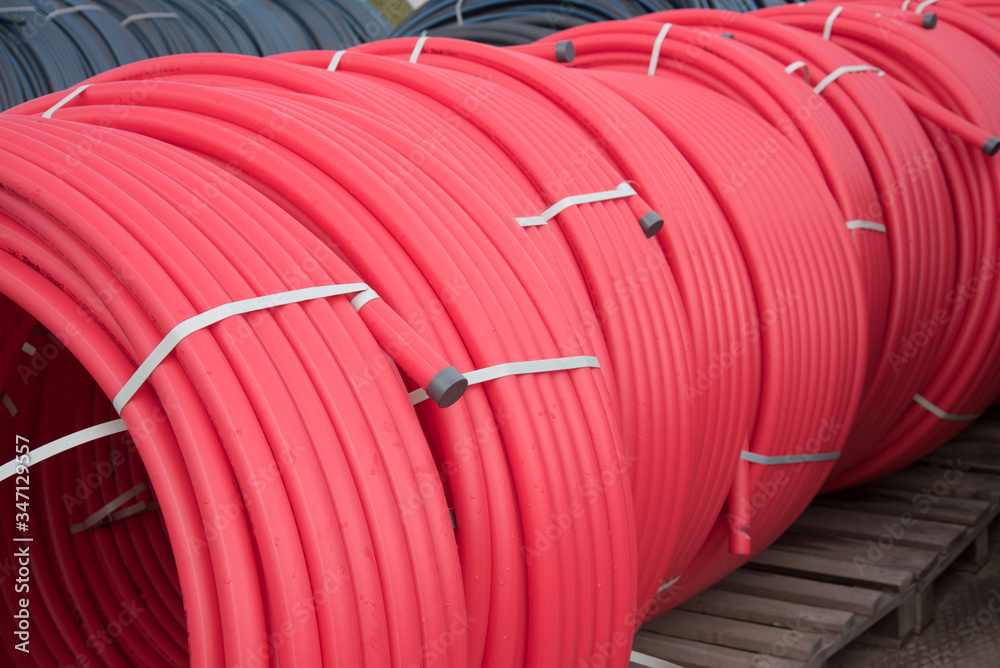 Fototapeta premium Red plastic pipes rolled into open air rolls. Construction site