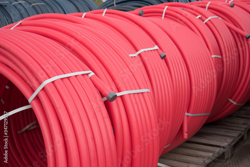 Red plastic pipes rolled into open air rolls. Construction site