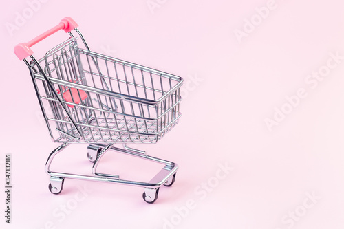 Small empty shopping cart on a pink background, copy space, horizontal