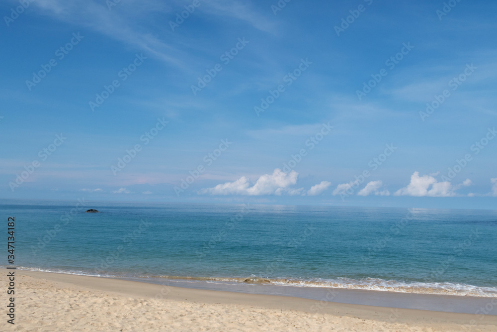 Beautiful sandy beach with calm ocean water surface with soft wave reaching seashore in sunny blue sky background with cotton candy clouds & fluffy cumulus cloudscape at Andaman Sea, island paradise 