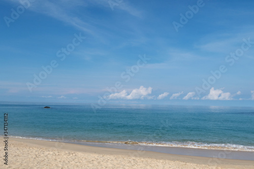 Beautiful sandy beach with calm ocean water surface with soft wave reaching seashore in sunny blue sky background with cotton candy clouds & fluffy cumulus cloudscape at Andaman Sea, island paradise  © BuaLily