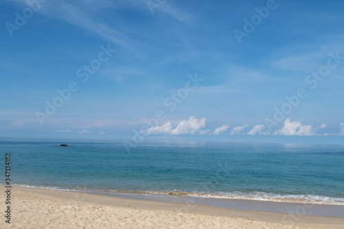 Beautiful sandy beach with calm ocean water surface with soft wave reaching seashore in sunny blue sky background with cotton candy clouds & fluffy cumulus cloudscape at Andaman Sea, island paradise 