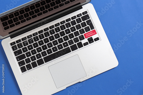 Modern laptop with quality control button on blue background, top view