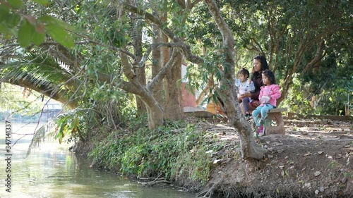 Little baby girls, sisters, sitting with mommy and learn to feed fishes in the pond with pieces of bread - spending time together, mother children bond