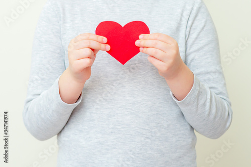 Closeup of hands of child holding red paper heart on white background. Red heart in child s hands.