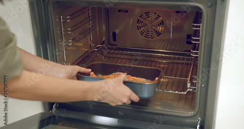 Close-up of female hands putting a tray of fish in the oven in the kitchen. Cooking. Healthy diet