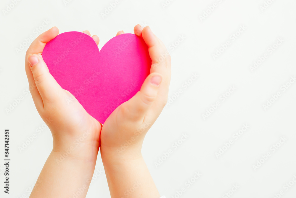 Closeup of hands of child holding paper pink heart on white background. Heart in hands with copy space.