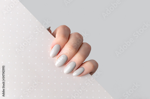 Beautiful womans hand with manicure close up on polka dot background. Gray nail polish