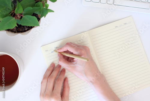 Top view of a young woman writes a day plan in a diary, sitting at a workplace with a computer. Home schooling, working at home concept