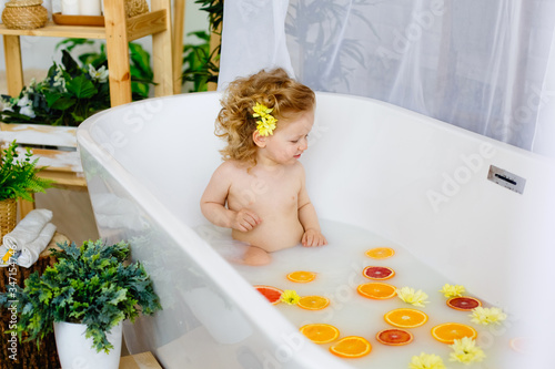 Child on the milk bath with flowersa little girl with curly hair in a milk bath with yellow flowers and orange oranges, red grapefruits. photo