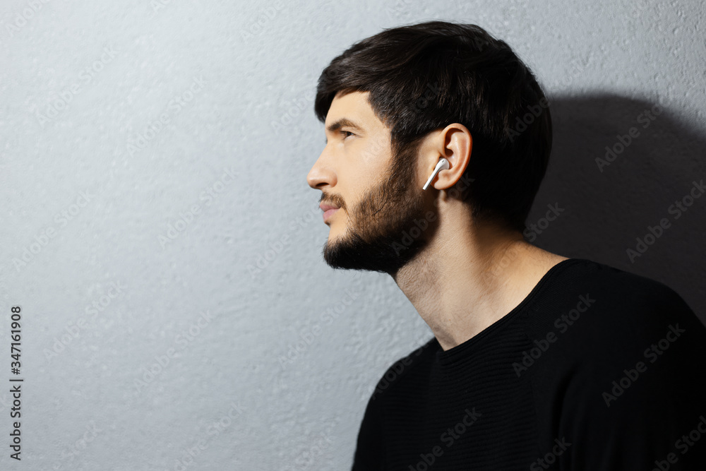 Fototapeta premium Profile portrait of young guy using wireless earphones on background of textured wall of grey.