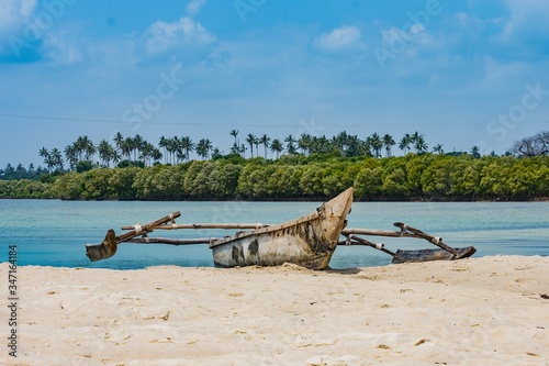 A canoe with its outrigger is resting at the shore of a river with a low tide thus isolated from the sea