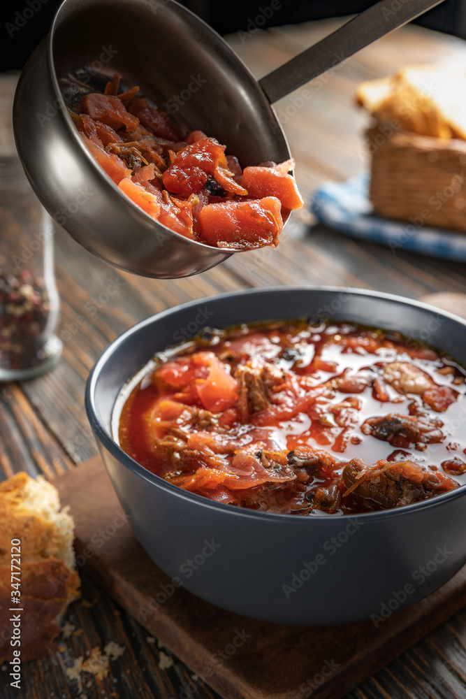 Borsch is poured into a bowl of soup ladle, traditional Ukrainian vegetable soup made from beets, carrots, tomatoes, potatoes, cabbage, herbs and garlic, close-up, shallow depth of field, selective Borsch is poured into a bowl of soup ladle, traditional Ukrainian vegetable soup made from beets, carrots, tomatoes, potatoes, cabbage, herbs and garlic, close-up, shallow depth of field, selective
