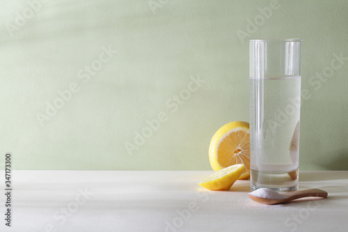 powdered Vitamin C on wooden spoon with glass of water and cut lemon on green and white background with shadow frow palm tree copy space photo
