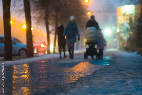 Fototapeta Naklejka Na Ścianę i Meble -  People silhouettes on the street of a night city in wet snow cold slippery winter rainy weather 