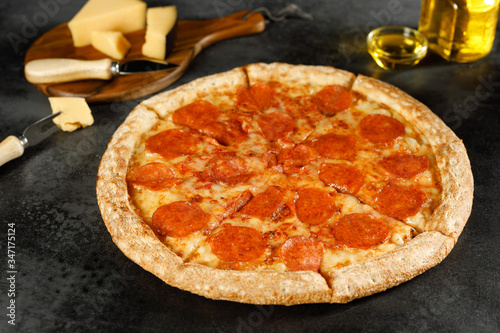 Pepperoni pizza on a black background with tomato butter and garlic in composition