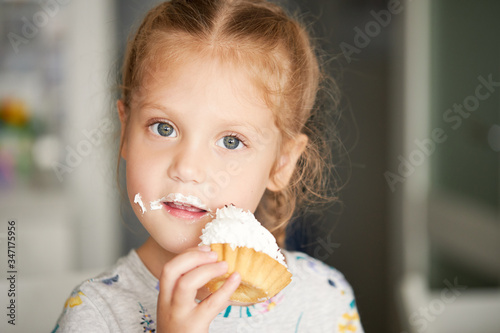 Cheerful smiling child girl eating a delicious cake and showing thumbs up. mouth in cream. Cheerful carefree childhood