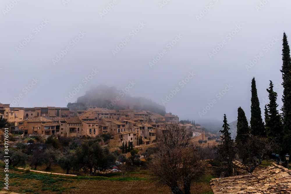 A picturesque panoramic view of the traditional buildings in the center of Alquézar (Huesca, Spain) on a hill covered by morning mist in winter A picturesque panoramic view of the traditional buildings in the center of Alquézar (Huesca, Spain) on a hill covered by morning mist in winter