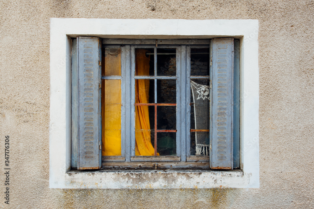 une vieille fenêtre aux rideaux métalliques bleus et un vieux rideau jaune dans une maison abandonnée