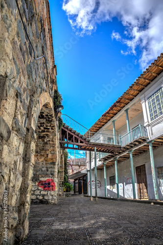 Old house in front of the ancient and famous stone Puente Roto  or Broken Bridge  on a sunny afternoon  Cuenca  Ecuador.