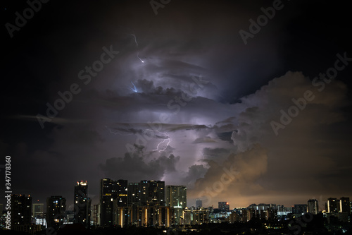 Thunder bolts striking through layers of clouds with tall buildings and city landscape in the foreground