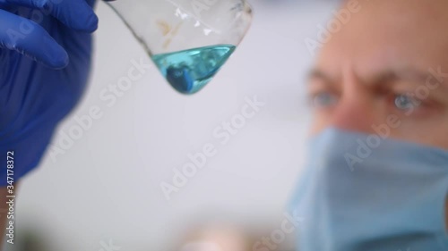 Young doctor in protective gloves looks at the medicine. Video with a blurry white background.
