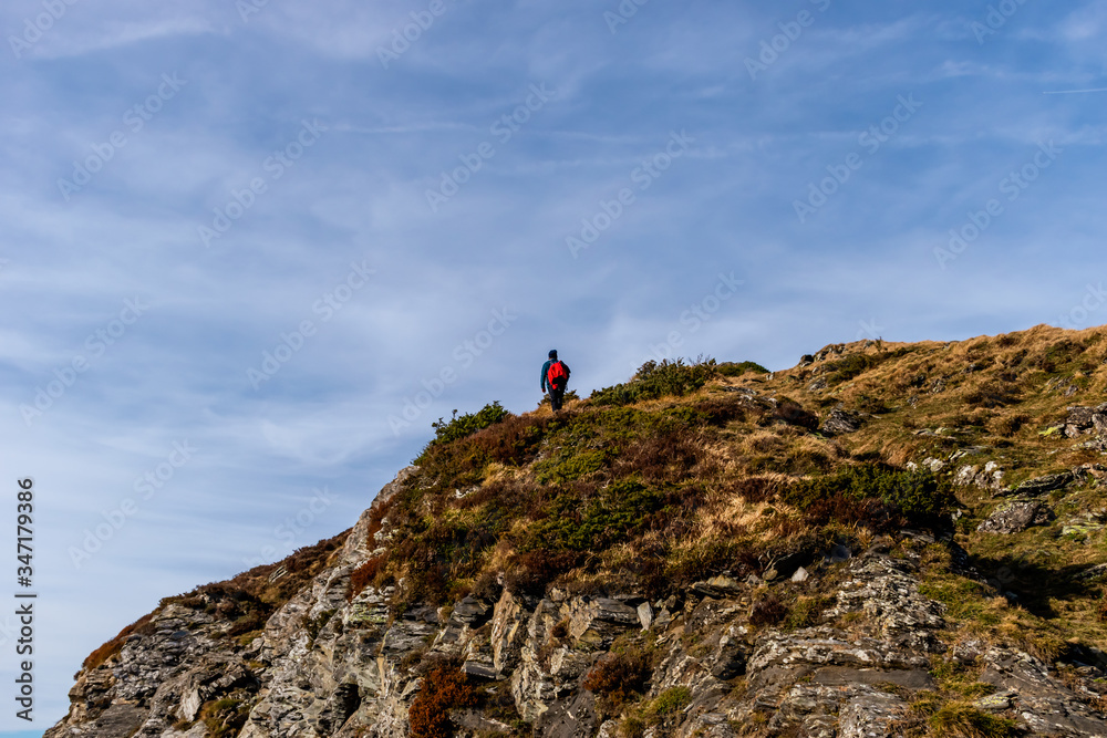 A full body shot of an unrecognizable male Caucasian hiker on top of a cliff in the French Pyrenees mountains during a hike