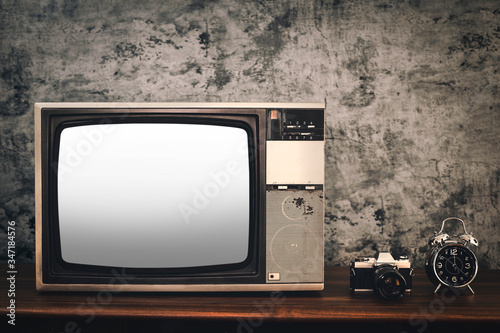 Retro old television with cut out screen, vintage camera and a clock on wooden table in front of old concrete wall background