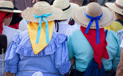 Back of anonymous women in traditional costumes at local festival in Gran Canaria, Spain. Popular celebration with people on wicker hats and colorful scarfs in Las Palmas city, Canary Islands photo