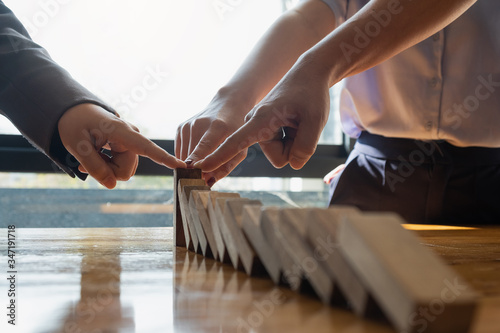 close up team businessman hand stopping falling wooden dominoes effect from continuous toppled or risk, strategy and successful intervention concept for business.
