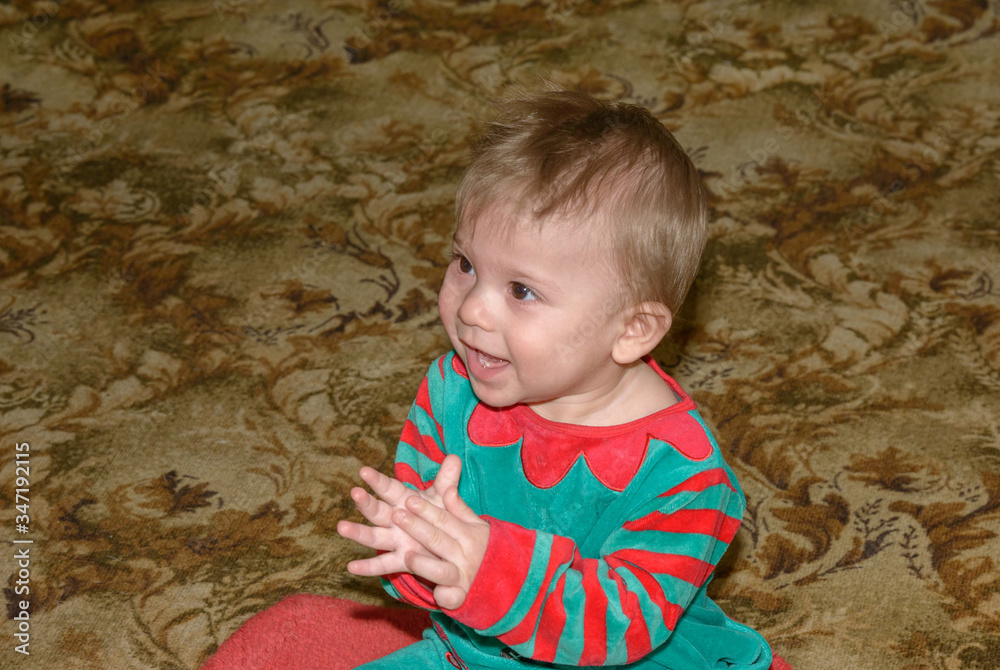 Fototapeta premium Baby boy in red-green suit is learning to play patty-cake.